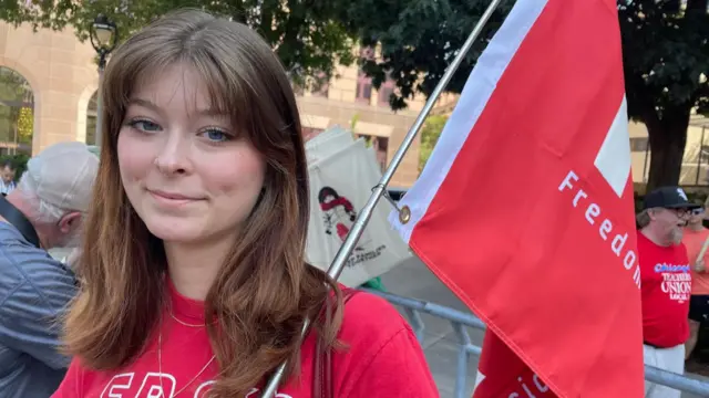 Gia Davila holds a flag while smiling at the camera at the protest