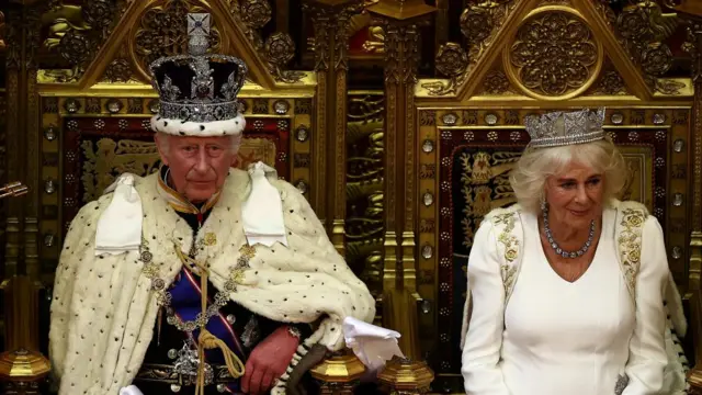 Britain's King Charles III, wearing the Imperial State Crown and the Robe of State, sits alongside Britain's Queen Camill