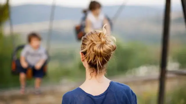 A woman watching two children on a swing