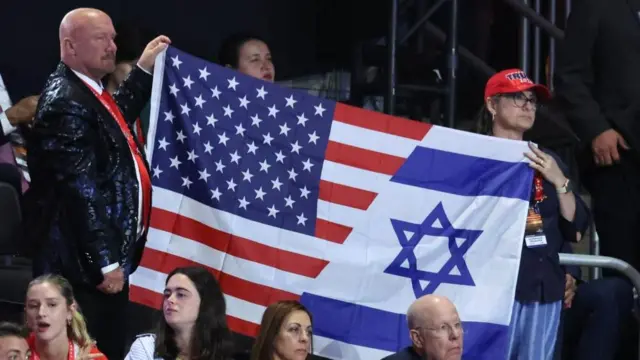 Crowd members hold up a flag of both the US and Israel