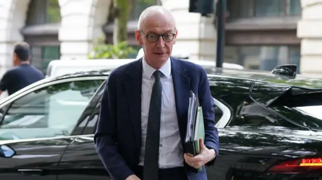 McFadden holds a bundle of folders as he walks towards the camera