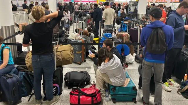 People sit on their suitcases as they wait at Gatwick