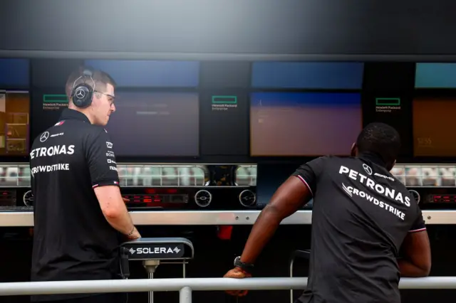 A Mercedes team member, whose shirt bears the logo of team sponsor Crowdstrike, looks on as Windows error screens are seen on their pitwall