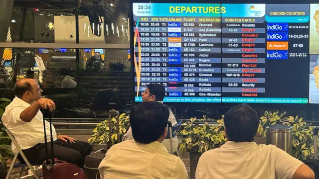 Three men look at a departure board where most of the flights say Delayed or Cancelled