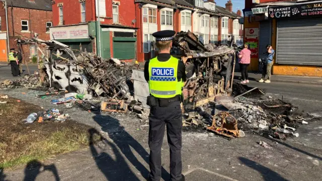 Police officer standing in front of burnt out bus