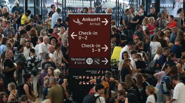 Loads of people walking while a sign stands in the middle of the floor pointing to check in an arrival gates at an airport