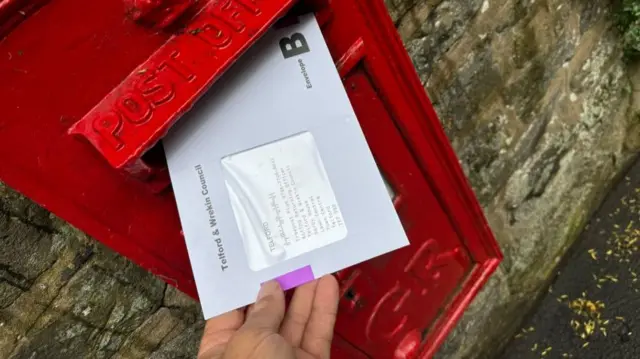 Pic shows a partial hand posting a letter into a red letterbox