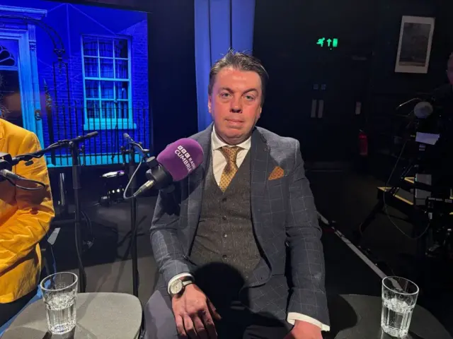 Reform UK candidate for Penrith and Solway Matthew Moody sits in the ˿ Cumbria election debate studio wearing a check suit and a grey waistcoat