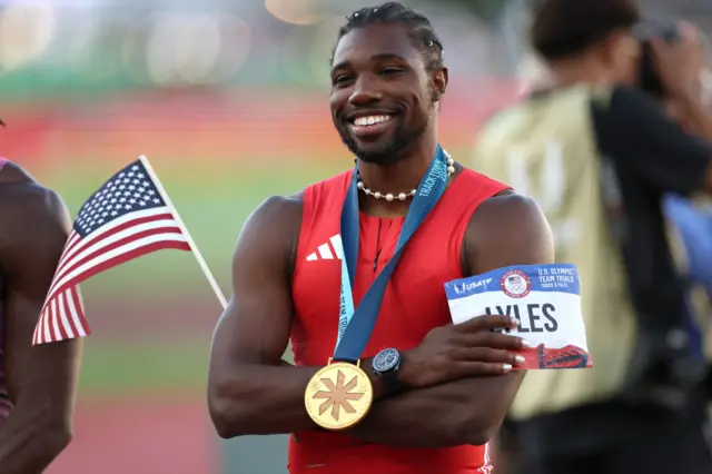 Noah Lyles wears a gold medal and holds an American flag