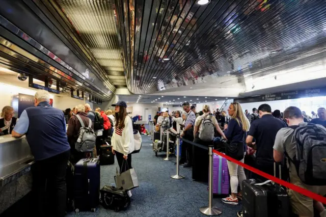 Passengers holding luggage queue for the check-in desks