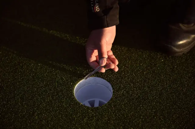 A greenkeeper uses scissors to cut the grass around a hole on a green at Royal Troon