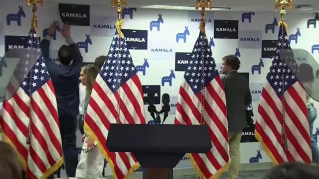 people in suits stick paper to a banner behind a lectern