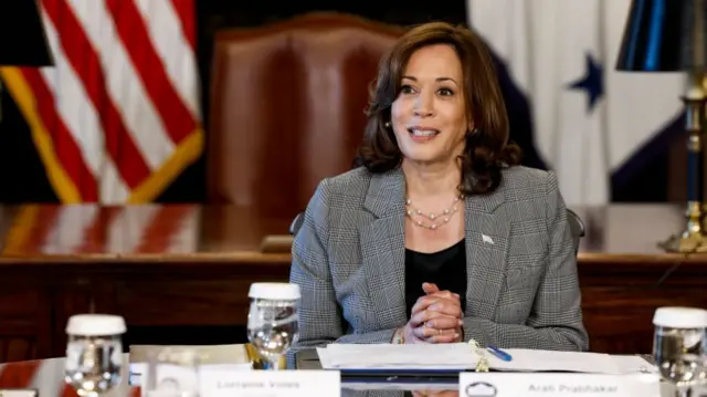 Kamala Harris, wearing a grey jacket, sat at a desk