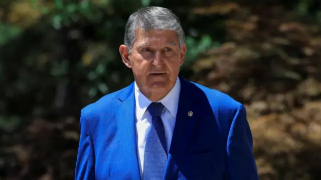 Joe Manchin standing outside in the sunshine, he's wearing a suit and looking off to the right of the camera