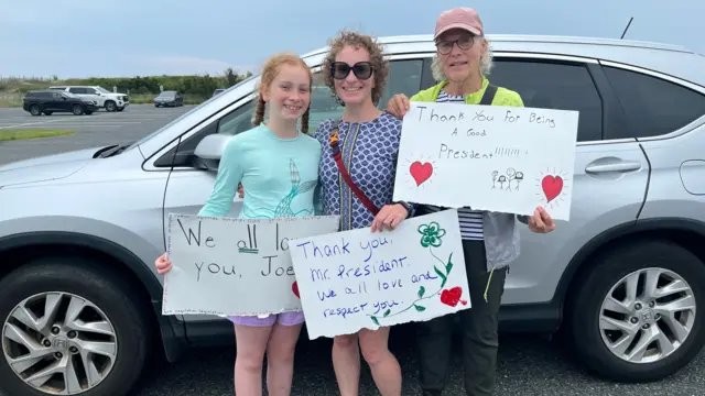 Three women hold signs bearing various thank you messages to Joe Biden