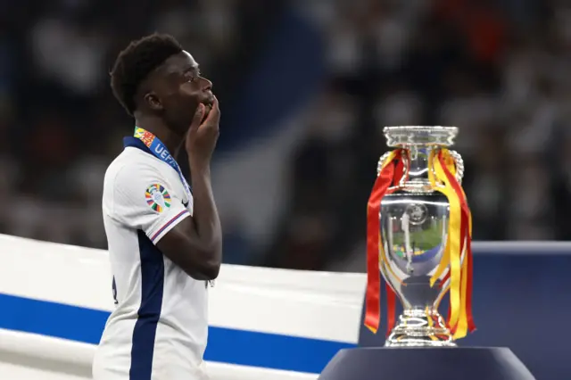 Bukayo Saka next to the European Championship trophy, dressed in Spain colours
