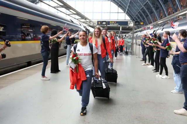 Becky Downie leads a line of Team GB athletes down the platform at a train station