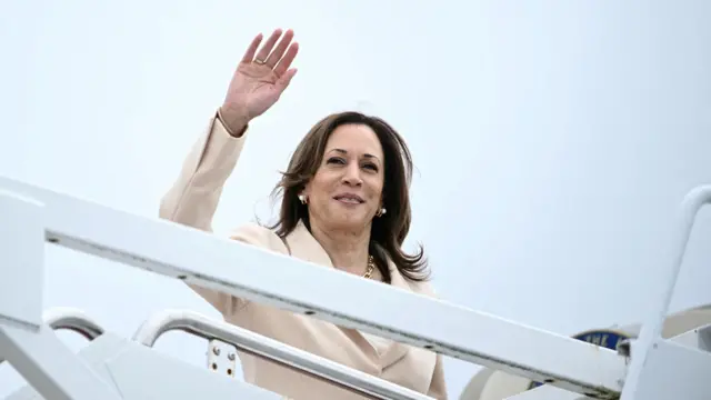 Kamala Harris wears a beige suit and waves from an airplane