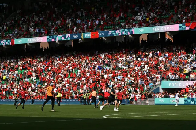 Fans run on the football pitch at the Olympics