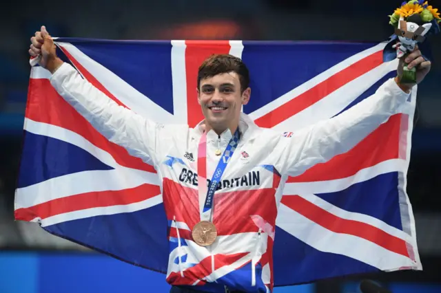 Tom Daley holds out a Union Jack and wears a bronze medal around his neck