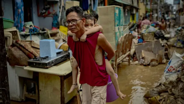 A resident carries a child past muddied homes after they were flooded by Typhoon Gaemi on July 25, 2024 in Marikina, Metro Manila, Philippines.