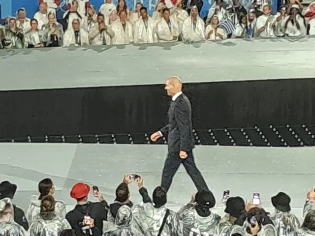 Zinedine Zidane walks along the stage while onlookers take photos.