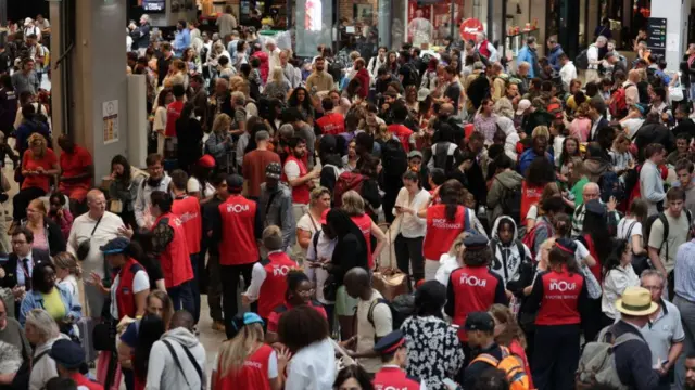 Overhead image with SNCF workers wearing jackets speaking to crowd of passengers