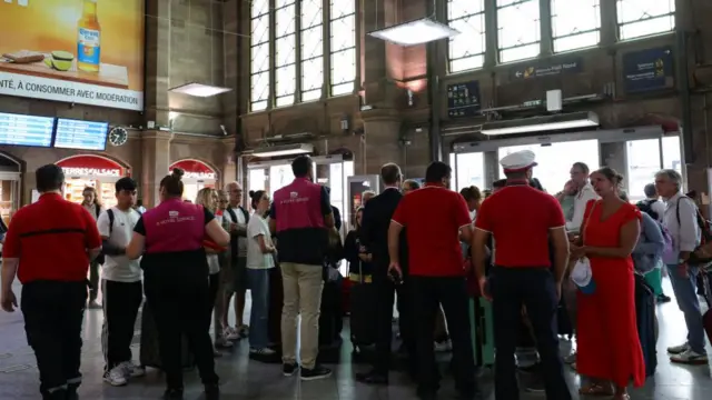 Shot from behind featuring SNCF workers wearing red speaking with passengers