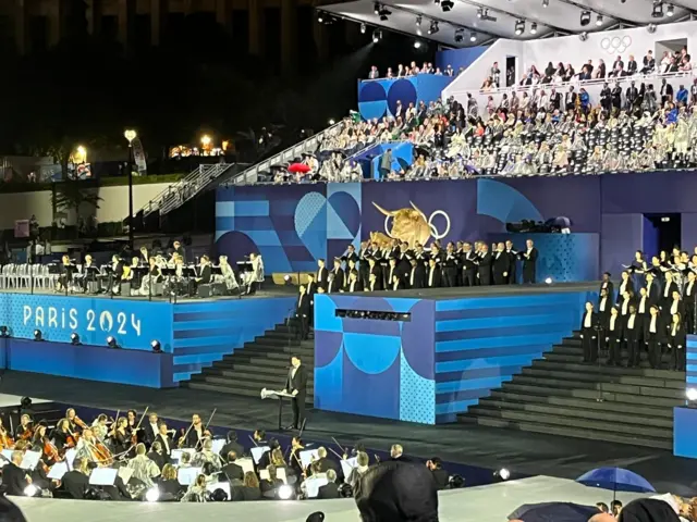 Musicians standing on a stage wearing formal clothes of white short and black suit.