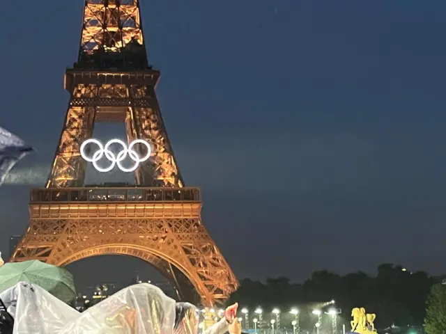 Eiffel Tower lit up in warm lights and with a large white Olympic rings display on it.