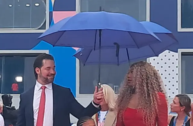 Alexis Ohanian holding an umbrella for Serena Williams