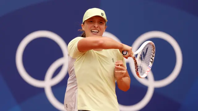 Iga Swiatek plays a shot in practice with the Olympic rings in the background