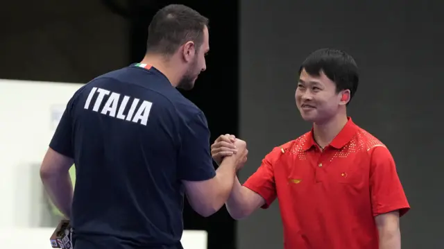 Federico Nilo Maldini of Italy congratulates Yu Xie of China after men's 10m air pistol final at 2024 Paris Olympics