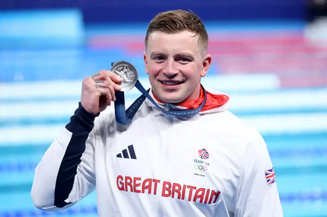 Adam Peaty holds up a silver medal