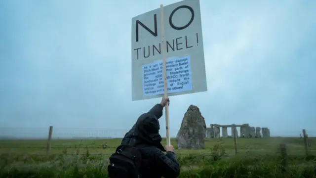 A protester holds a sign that reads 'no tunnel' by the Stonehenge monument