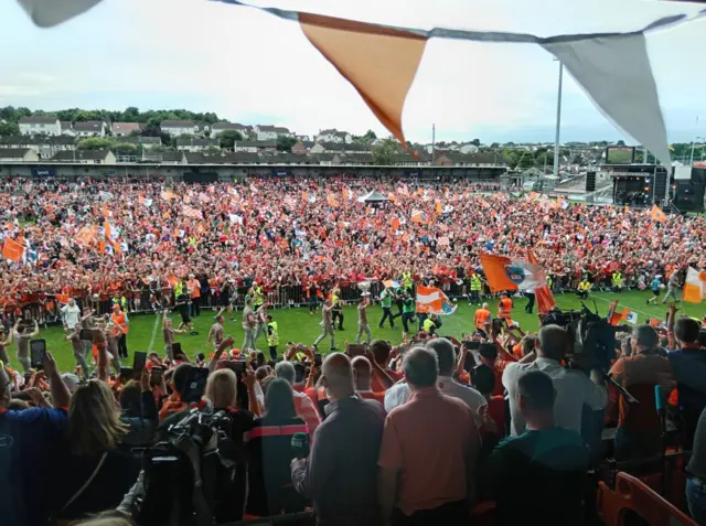 Crowds in orange and white with players carrying a silver trophy