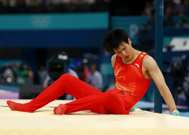 Weide Su sits on the floor after falling off the high bar