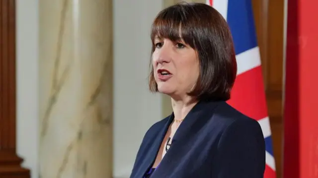 Labour chancellor Rachel Reeves speaking at an indoor event with a partial British flag in the background