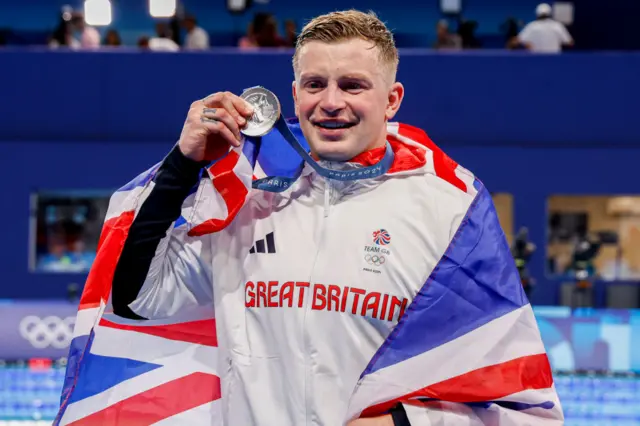 Adam Peaty holds up his silver medal