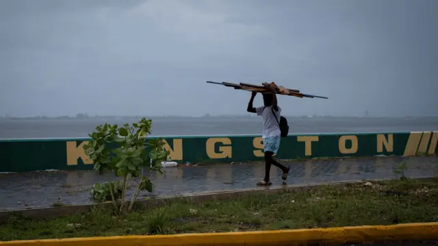 A man walks down a pavement carrying wood on his head as Hurricane Beryl approaches, in Kingston, Jamaica.