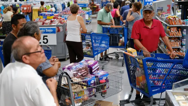 People queue with full shopping trolleys at supermarket checkouts