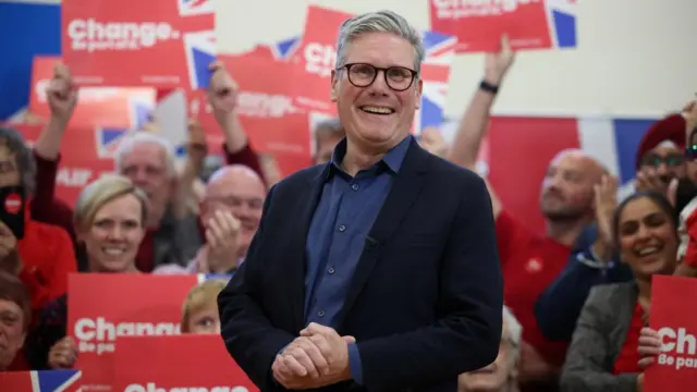 Keir Starmer smiles, behind him supporters hold signs that read "change"