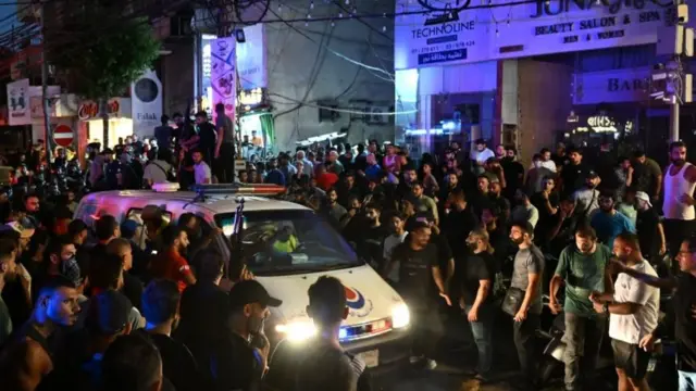 Crowds of people gather round an emergency van on a street in Beirut