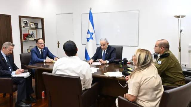 Benjamin Netanyahu siting around a table with officials and a soldier in uniform