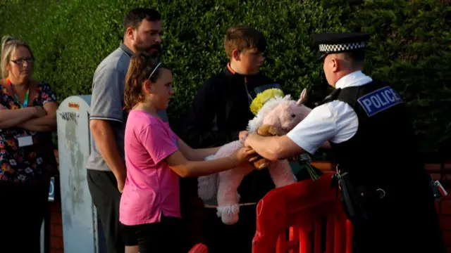 A police officer receives flowers and a stuffed animal from local residents to put them behind the police cordon near the scene of a stabbing