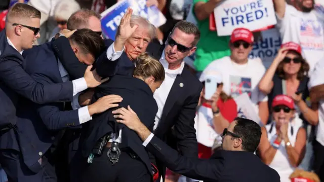 Republican presidential candidate and former U.S. President Donald Trump gestures with a bloodied face while he is assisted by U.S. Secret Service personnel after he was shot in the right ear during a campaign rally at the Butler Farm Show in Butler, Pennsylvania, U.S., July 13, 2024