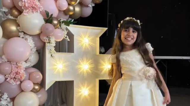 Alice stands smiling next to a cross studded with lights