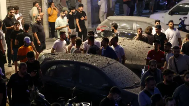 PEople stand around cars covered in dust and debris