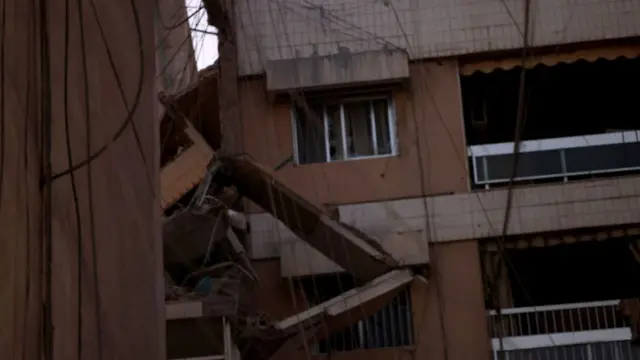 A partially destroyed building with masonry and wires hanging down