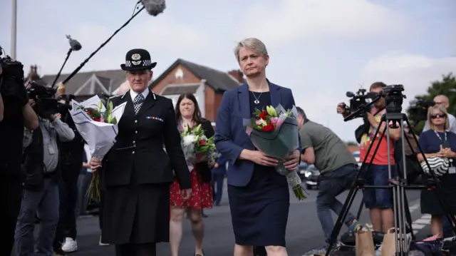 Yvette Cooper wearing a dress and blazer holding flowers and a blazer